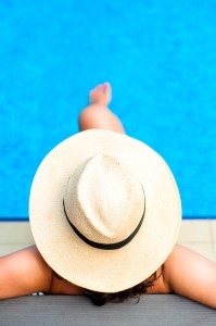 Woman with beach hat relaxing by the pool