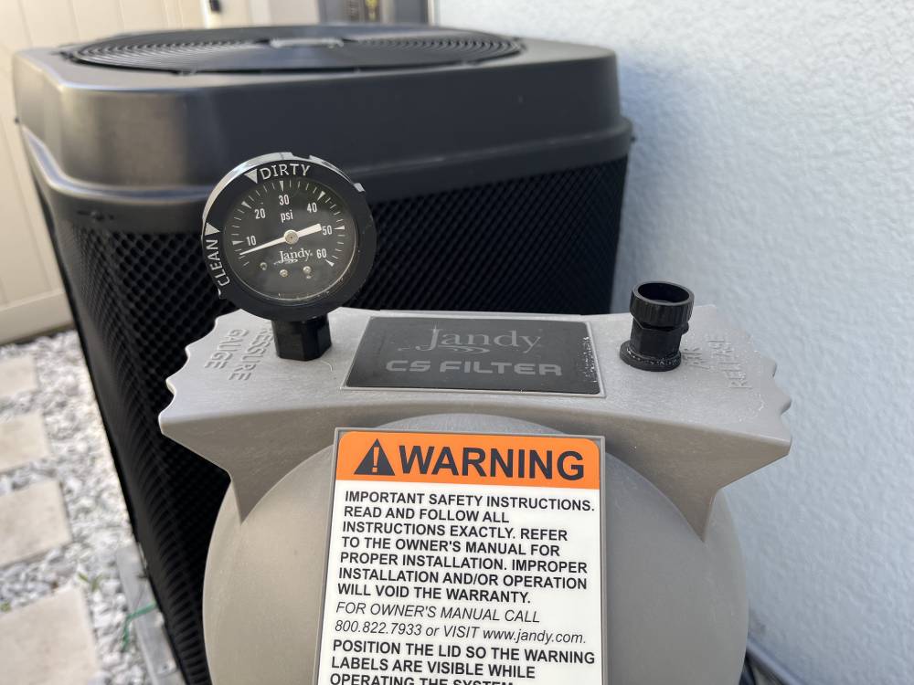Close-up of a Jandy CS filter with a pressure gauge showing "dirty" and "clean" indicators, and a warning label instructing users to read safety instructions.