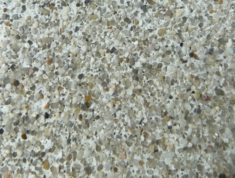 Close-up view of a textured concrete surface with small, mixed-colored pebbles embedded throughout.