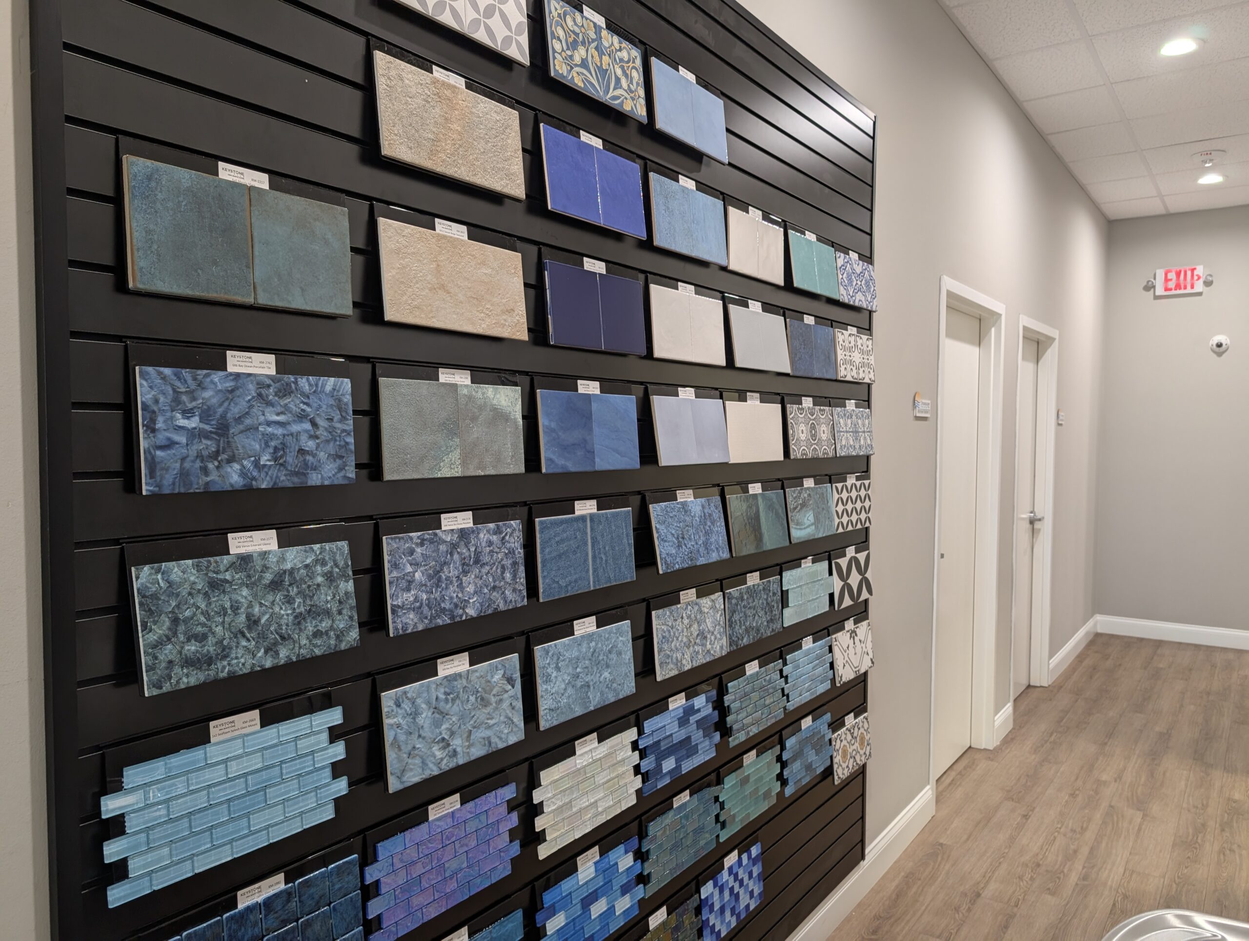 A display wall with various blue and beige tile samples arranged in rows in a showroom with light-colored walls and wood flooring.