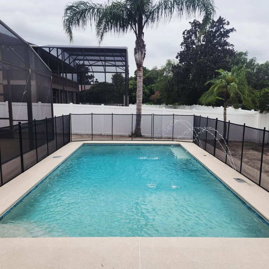 Rectangular swimming pool with clear water, built by expert Pool Builders in Lake Nona, surrounded by a safety fence, palm trees, and a white privacy fence in a backyard.