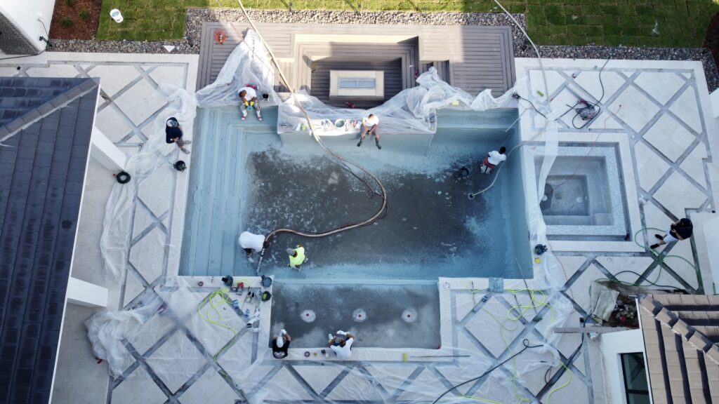 Aerial view of Pool Contractors in Orlando cleaning and renovating an empty rectangular swimming pool, with plastic sheets covering surrounding surfaces.